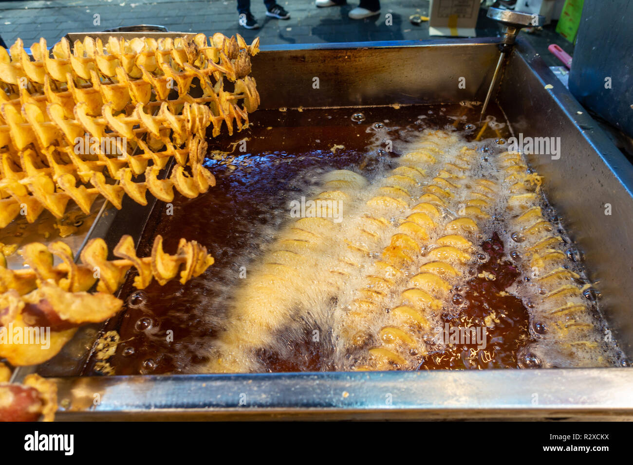 Spirali di patate su spiedini di legno friggere in olio ben caldo su un cibo di strada in stallo a Myeongdong a Seul, in Corea del Sud. Foto Stock