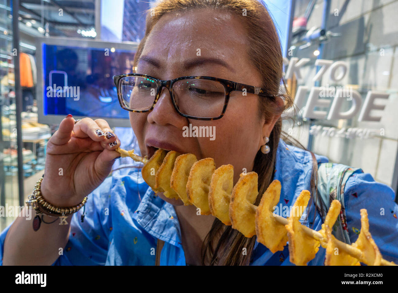 Una signora che mangia una profonda sparato a spirale di patate su un bastone comprato formano un cibo di strada in stallo a Myeongdong a Seul, in Corea del Sud. Foto Stock