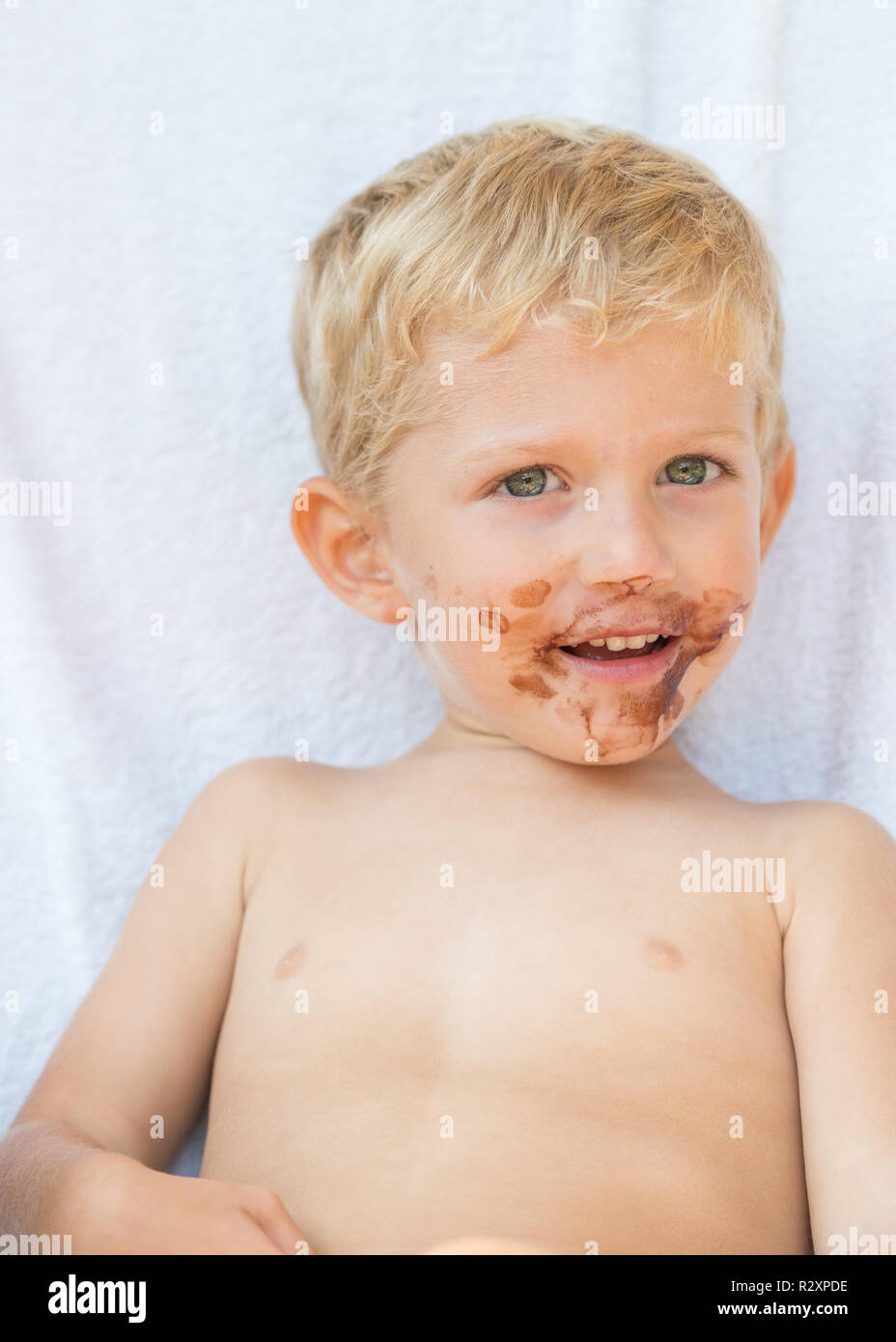 Ritratto del biondo baby boy con cioccolato sul suo volto isolato su sfondo bianco. Foto Stock