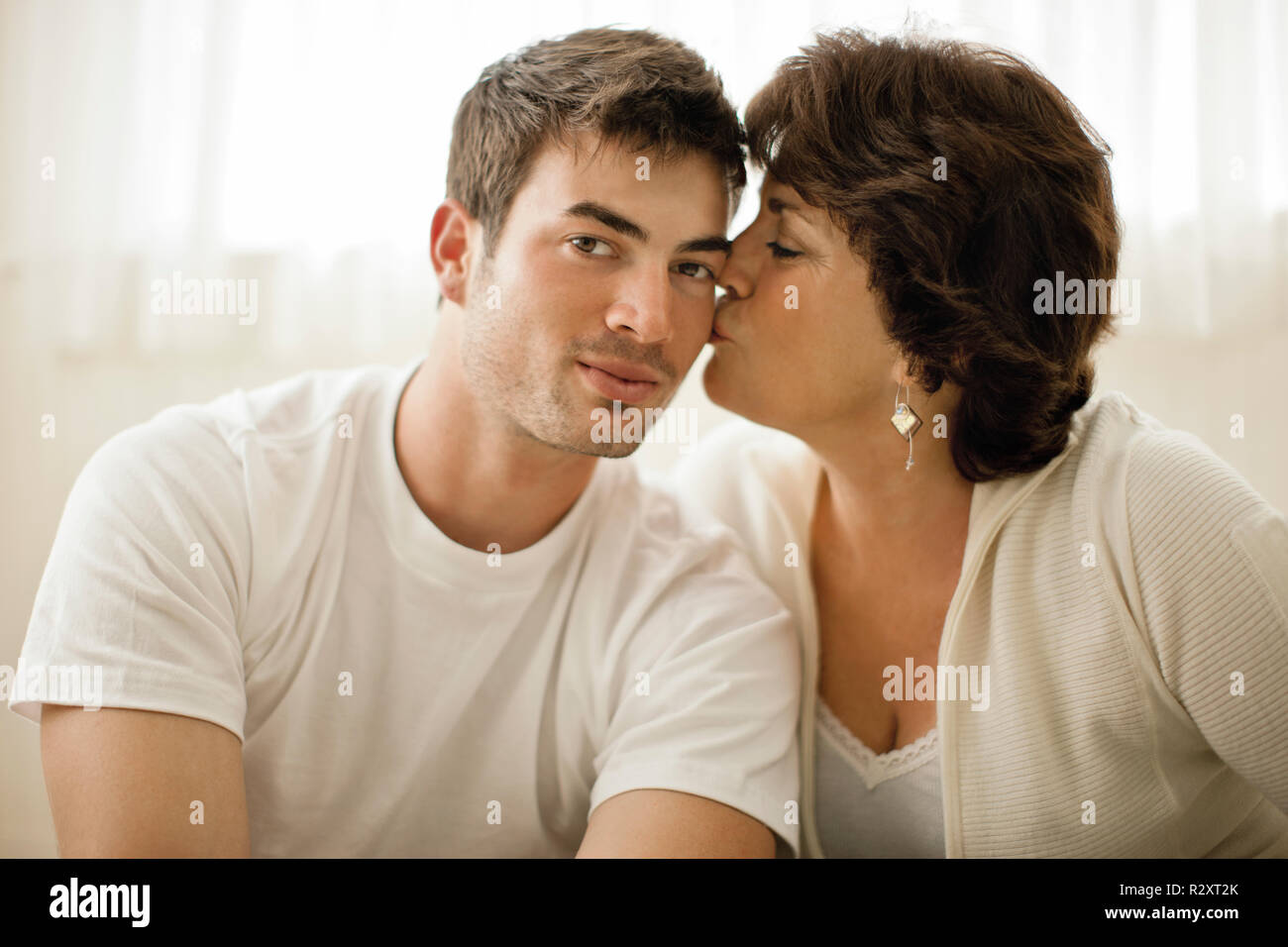 Ritratto di un giovane uomo baciato sulla guancia da sua madre. Foto Stock