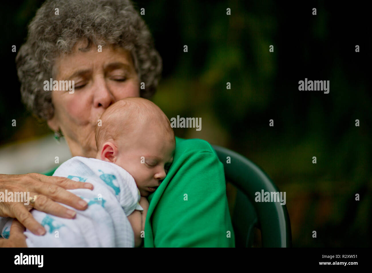 Senior donna seduta e tenendo un neonato in un cortile. Foto Stock