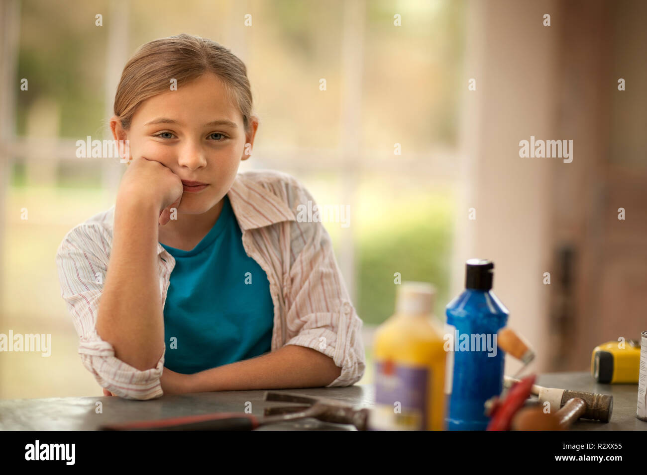 Ritratto di una ragazza contemplativa appoggiato su un banco di lavoro pieno di strumenti artigianali all'interno di un garage. Foto Stock