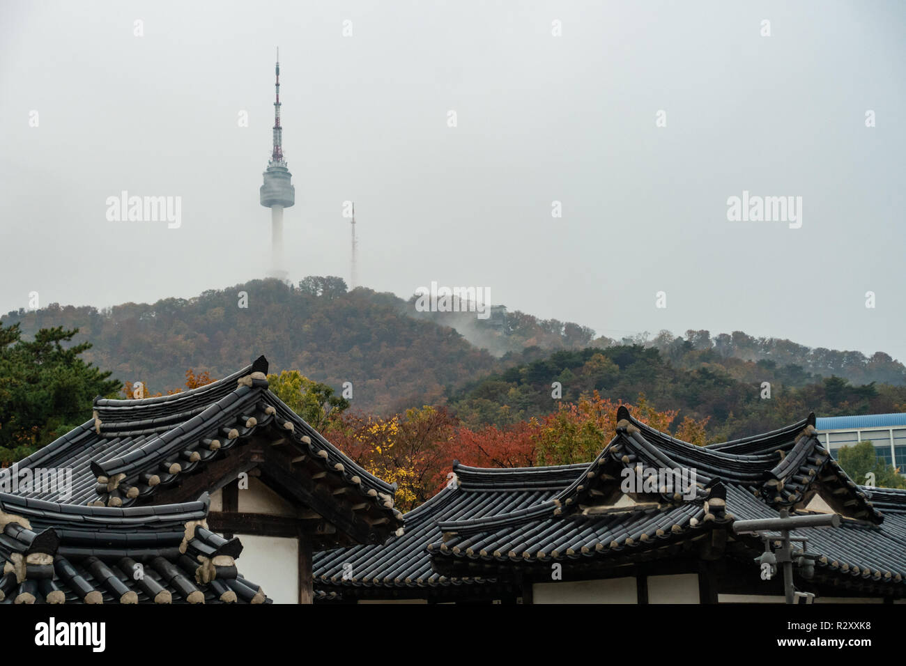 Una vista della Torre di Namsan parzialmente oscurata da nuvole vedere sui tetti delle case a Namsangol Villaggio Hanok, Seoul, Corea del Sud Foto Stock