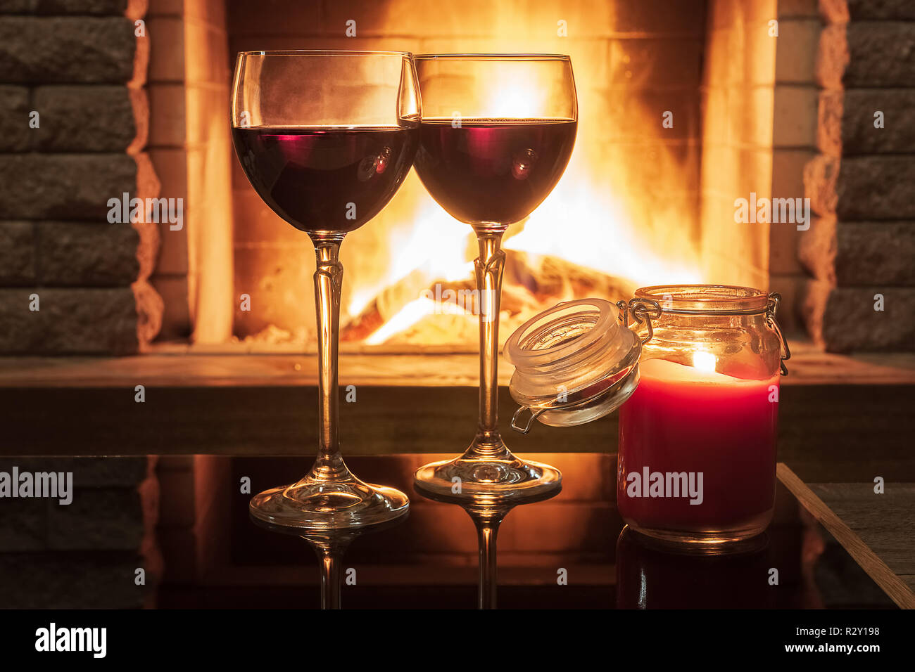 Scena tranquilla prima di un accogliente caminetto, con due bicchieri di vino rosso e candela, in country house in vacanza invernale. Foto Stock