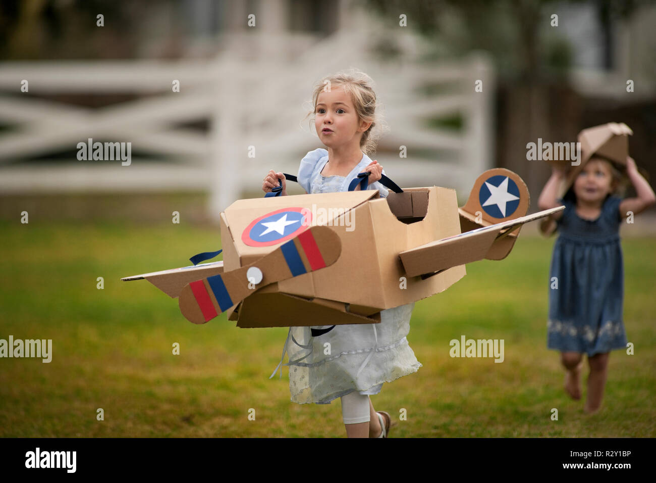 Due bambine divertirsi giocando con scatola di cartone aerei sul prato. Foto Stock