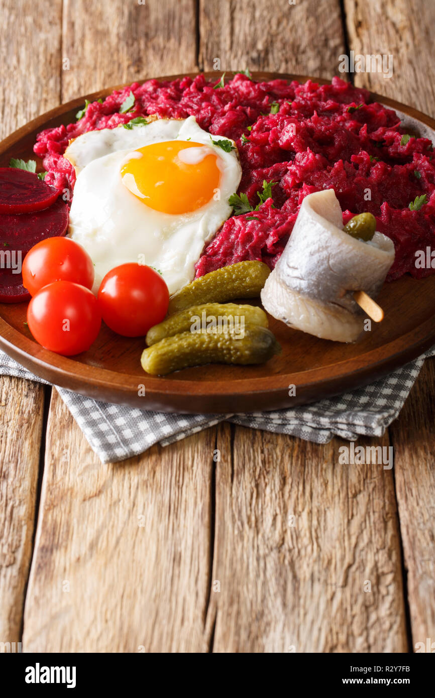 Labskaus tedesco sostanziosa pietanza di fecola di patate, di corned beef e barbabietola con uovo fritto, sottaceti e aringhe close-up su una piastra sul tavolo. In verticale Foto Stock