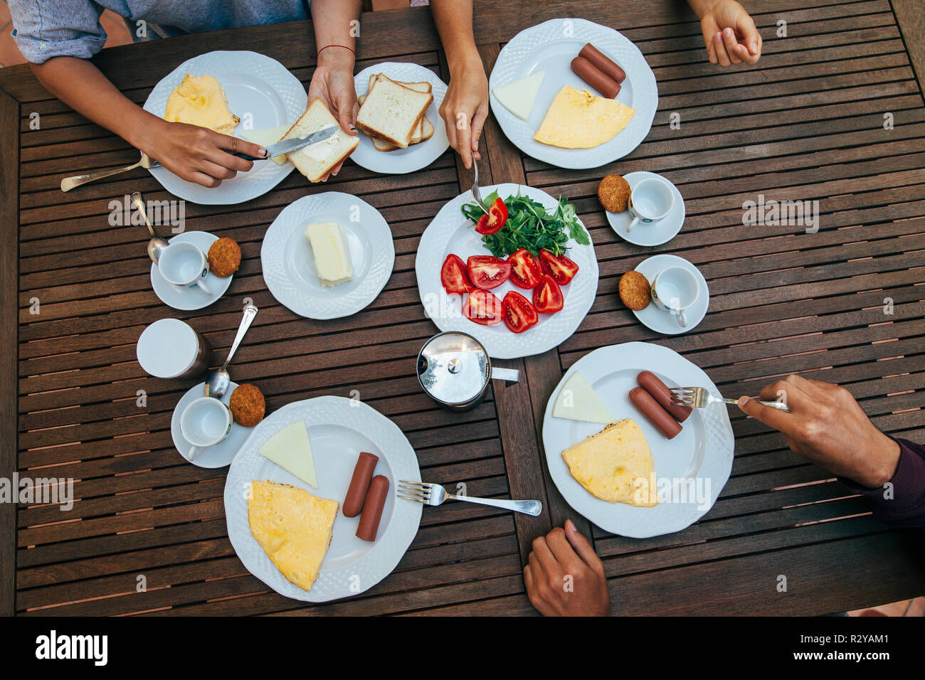 Gustando la prima colazione con gli amici. Vista dall'alto del gruppo di persone aventi pasto insieme mentre seduti a tavola in legno rustico Foto Stock