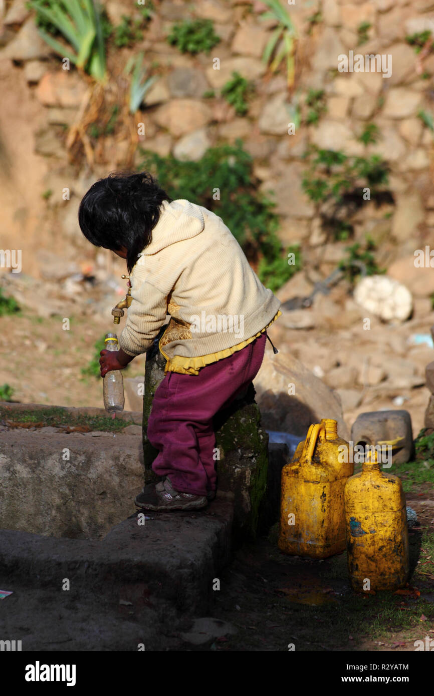 Giovane bambino indigeno che riempie la bottiglia di plastica con l'acqua del rubinetto nel villaggio rurale andino, Bolivia Foto Stock