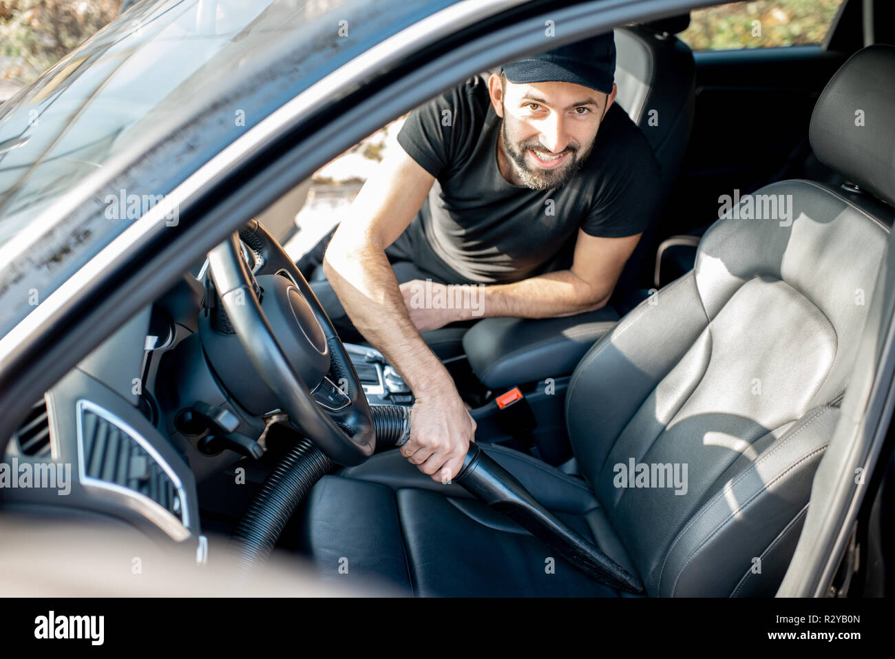 Pulitore professionale in black t-shirt e cappuccio di aspirare i sedili in  pelle di un auto di lusso Foto stock - Alamy