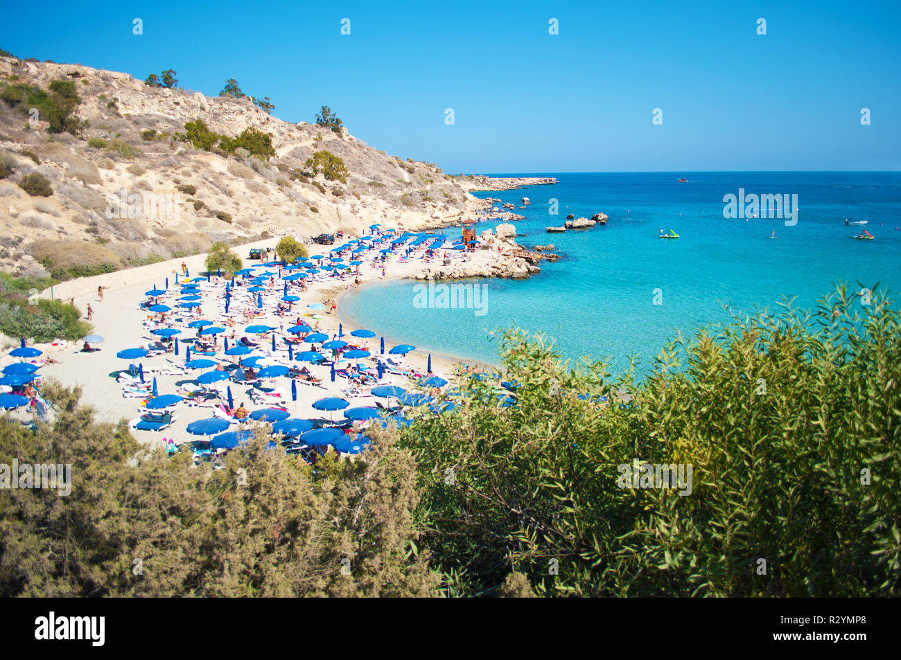 Immagine di Konnos spiaggia nei pressi di Agia Napa, Cipro. Blu molte sedie a sdraio e ombrelloni sulla sabbia bianca nei pressi di blu trasparente di acqua in una baia e le colline rocciose. Foto Stock