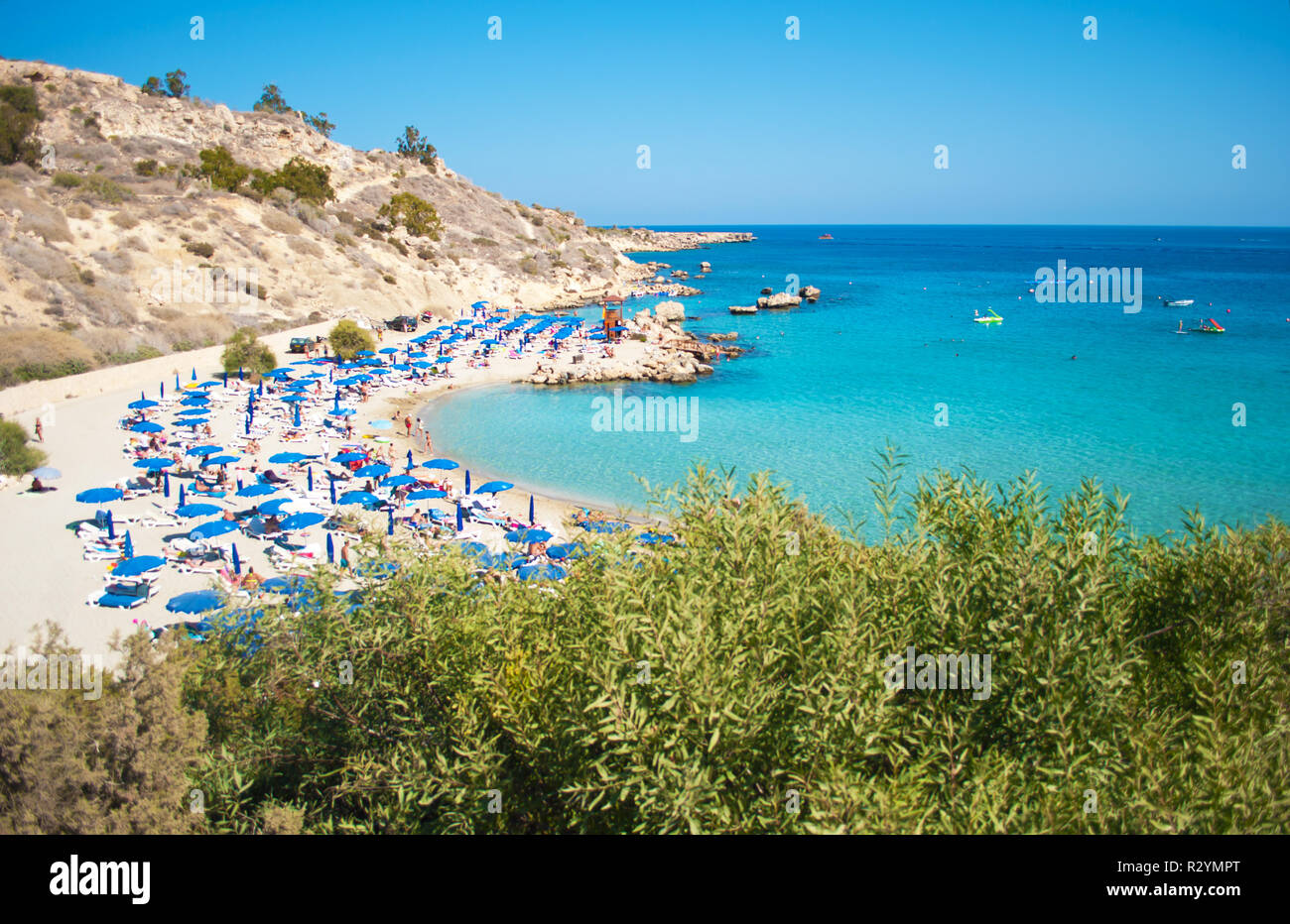 Immagine di Konnos spiaggia nei pressi di Agia Napa, Cipro. Blu molte sedie a sdraio e ombrelloni sulla sabbia bianca nei pressi di blu trasparente di acqua in una baia e le colline rocciose. Foto Stock