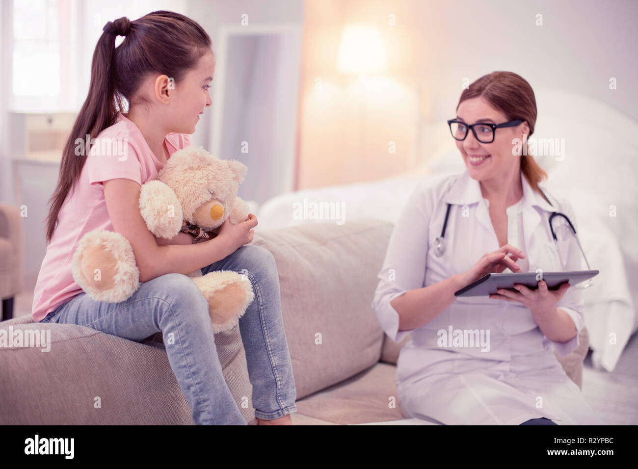 Famiglia professionale medico visita carina ragazza seduta sul divano con toy Foto Stock