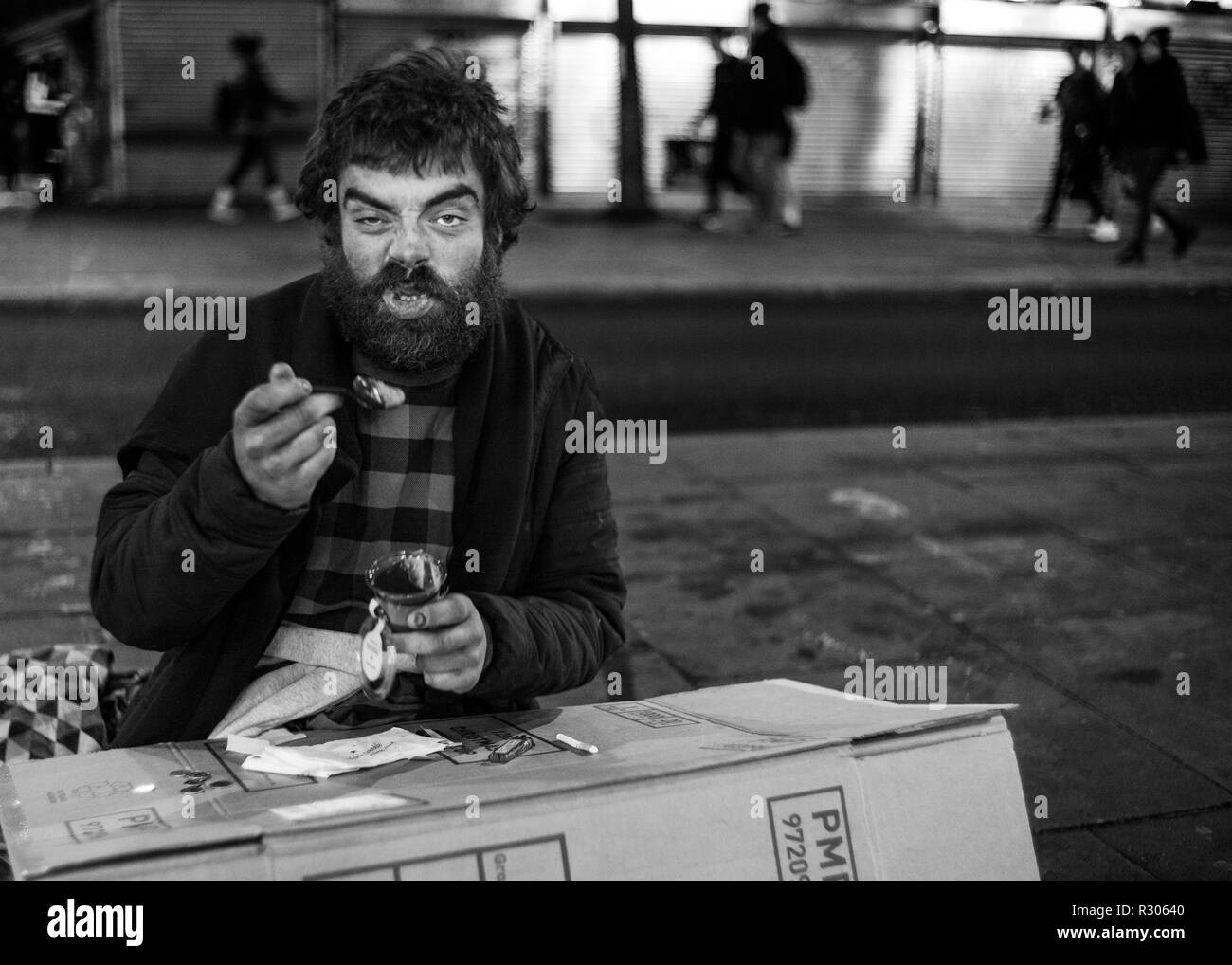 Senzatetto uomo seduto sulla strada di Londra mangiare di una scatola di cartone Foto Stock