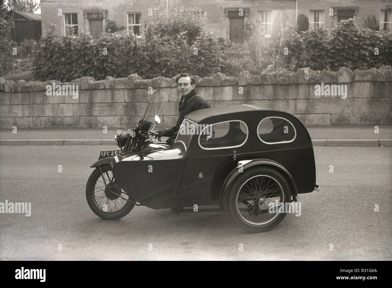 1950, storico, uomo sulla motocicletta con "coperto" Watsonian sidecar. Negli anni quaranta e cinquanta, questa forma di trasporto, spesso chiamato "combinazione" o "rig", era un metodo popolare per il trasporto di un passeggero fino a che la crescita di un'autovettura nella successiva parte del decennio. Eastablished nel 1912, il British sidecar Watsonian realizzati nel salutare, Birmingham è stata la più popolare sidecar nel suo giorno. Foto Stock