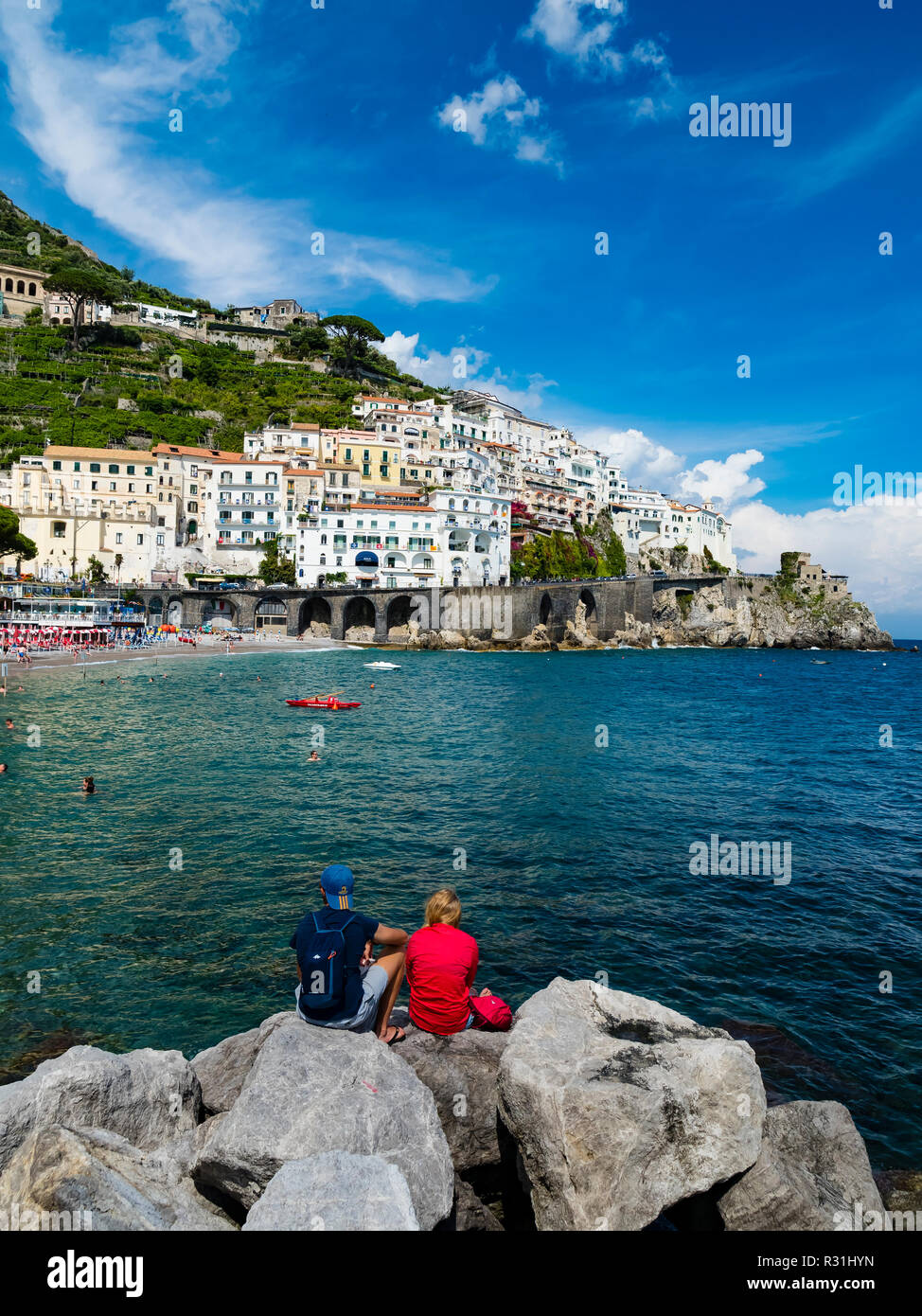 Giovane si siede sulla roccia e guarda la città vecchia e la Spiaggia di Amalfi, penisola di Sorrento, Costiera Amalfitana, Campania, Italia Foto Stock