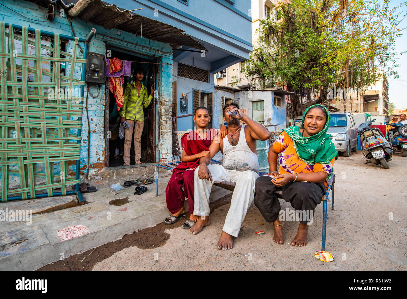 Un uomo con sua moglie e sua sorella sedersi in strada per una pausa di causalità, mentre un uomo sta alla porta. Ahmedabad, India Foto Stock