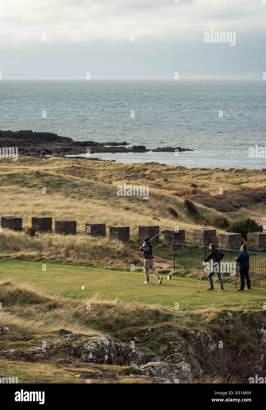 Tre uomini per giocare a golf in un corso sulla costa di East Lothian, Scozia, con vista al mare in background. In verticale Foto Stock