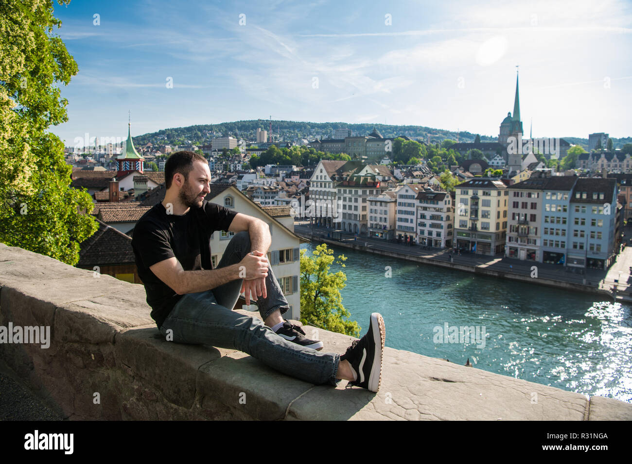 Bel giovane ragazzo seduto nel parco della città con una vista della città di Zurigo, Svizzera. Foto Stock