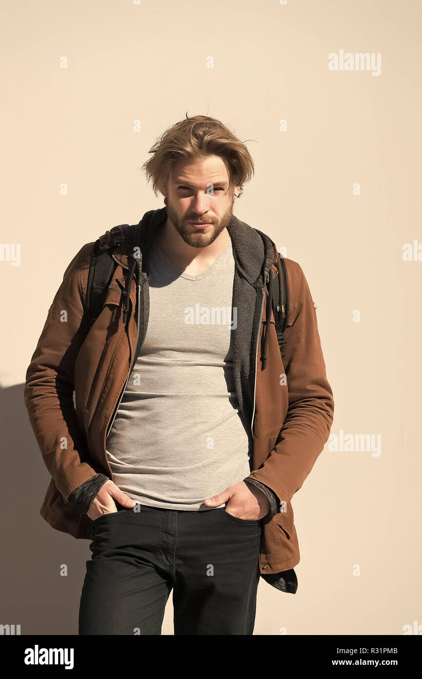 Macho con la barba sulla faccia di barba lunga e capelli biondi. Uomo di  usura cappotto marrone, tshirt, pantaloni sul muro grigio. Outfit, moda,  stile casual Foto stock - Alamy