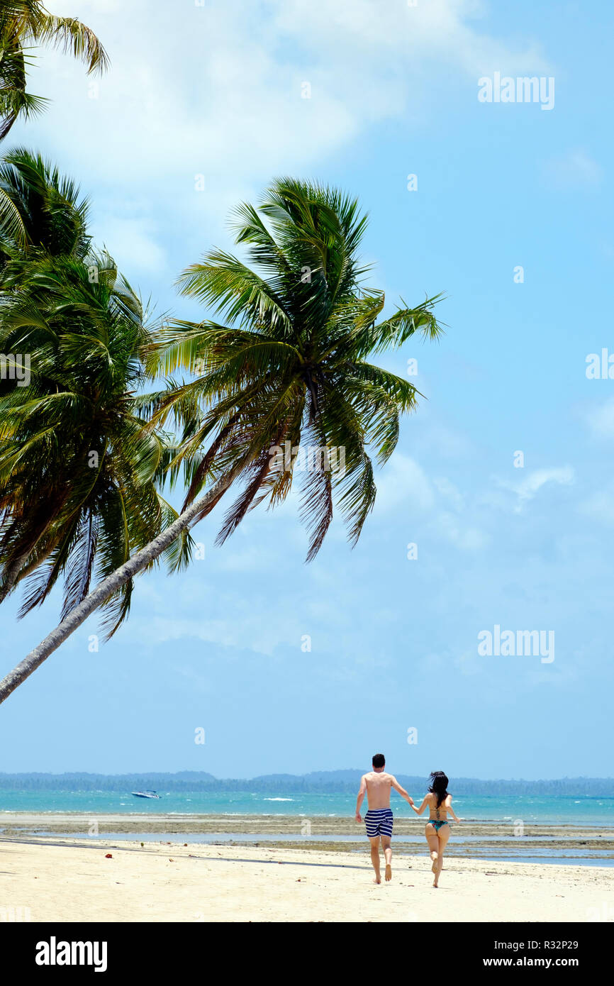 Un attraente coppia giovane che corre lungo un idilliaco, deserta spiaggia tropicale Foto Stock