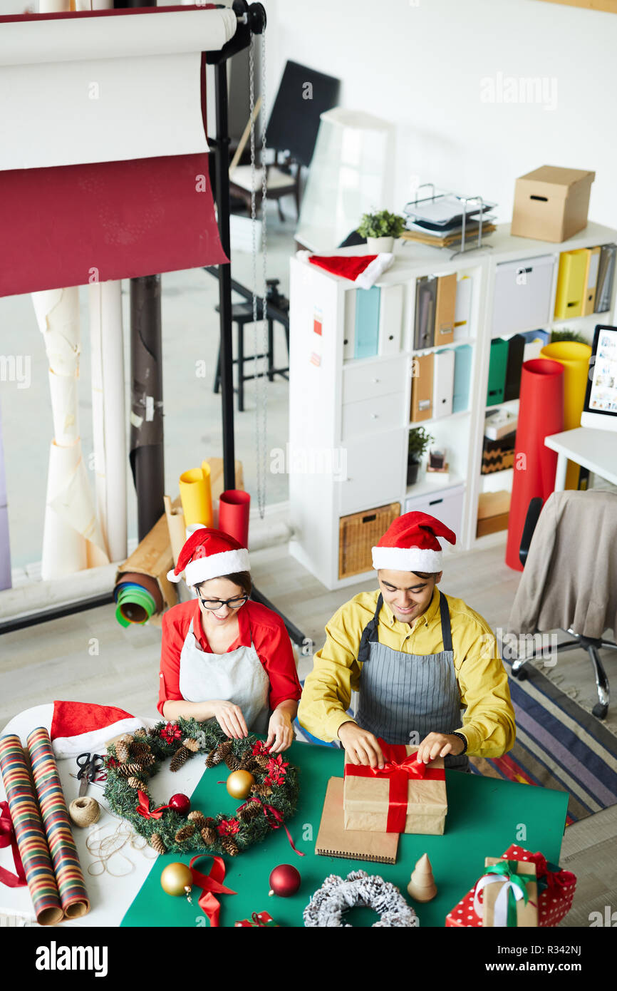 I giovani creativi l uomo e la donna a Santa caps rendendo pre-natalizio il lavoro in studio di design Foto Stock
