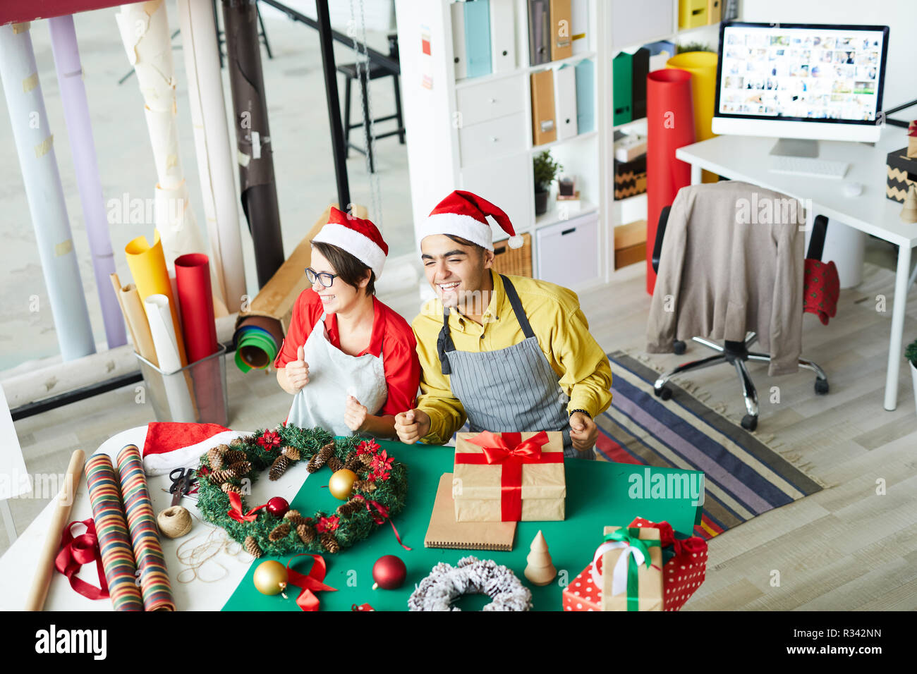 Giovane uomo e donna in Santa caps ridendo durante il lavoro prima del tempo di Natale Foto Stock