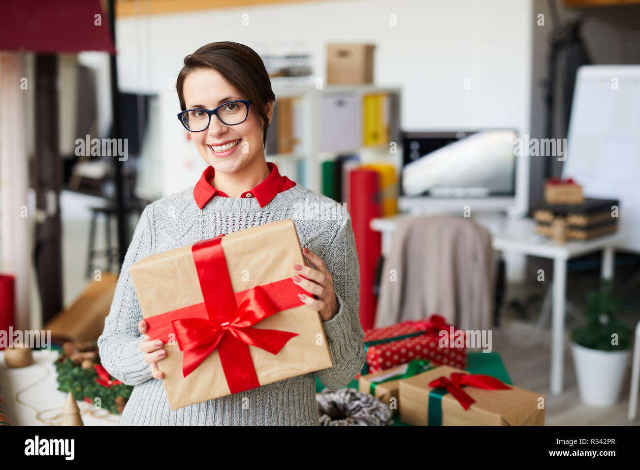 Imprenditrice casual con giftbox in piedi dal luogo di lavoro di design studio Foto Stock