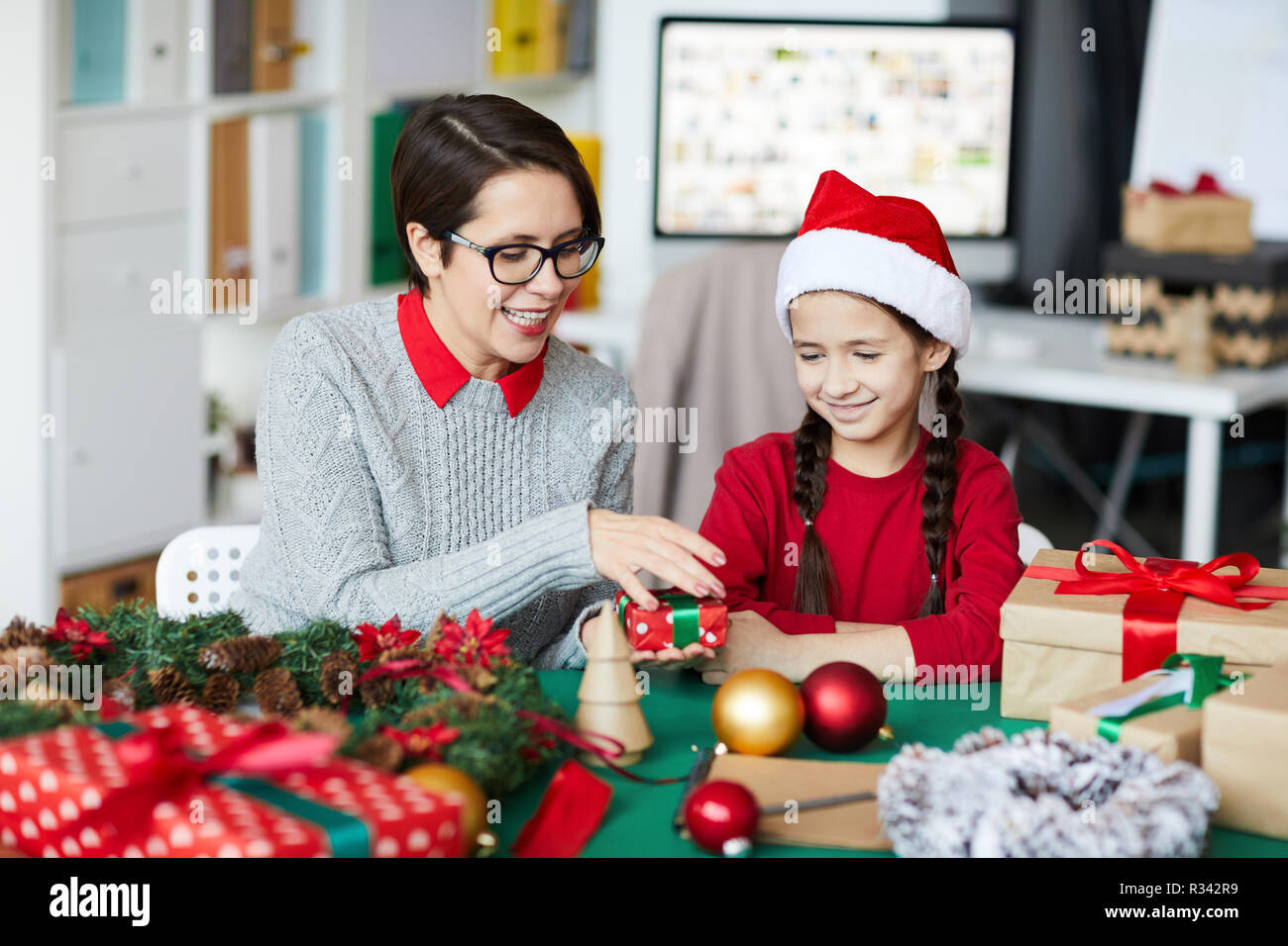 Giovane donna azienda piccola giftbox mentre mostra a sua figlia indossando Santa e cappuccio felpa rossa Foto Stock