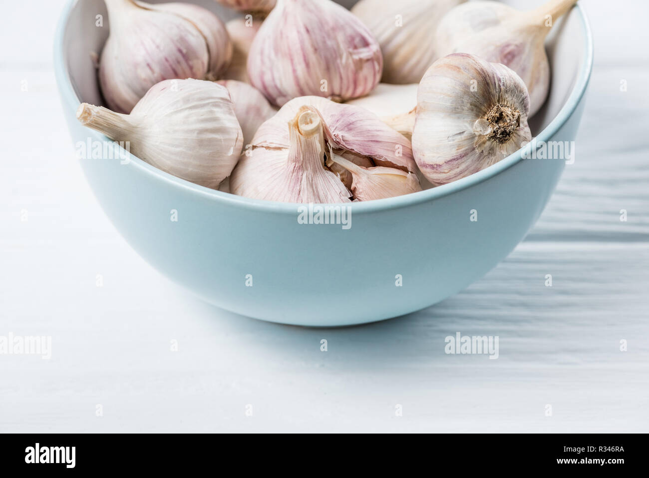 Teste d'aglio in ceramica blu ciotola di legno bianco tavolo da cucina Foto Stock