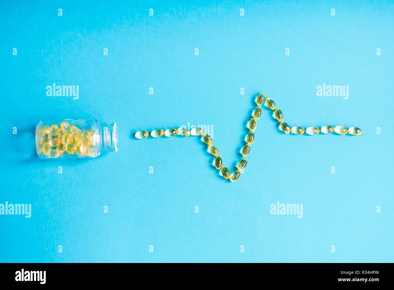 Le compresse di colore giallo sparse nella forma di un heartbeat da un vaso su uno sfondo blu. Pillole di problemi cardiaci Foto Stock