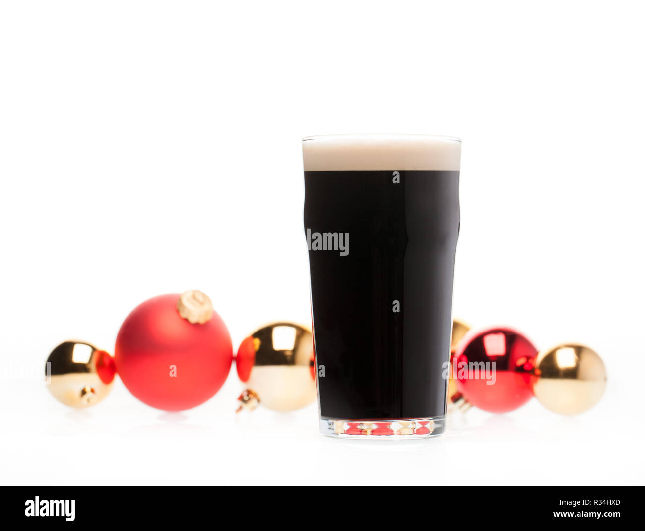 Completa di vetro pinta di birra scura o stout ale con sfocate baubles di natale in background su bianco Foto Stock