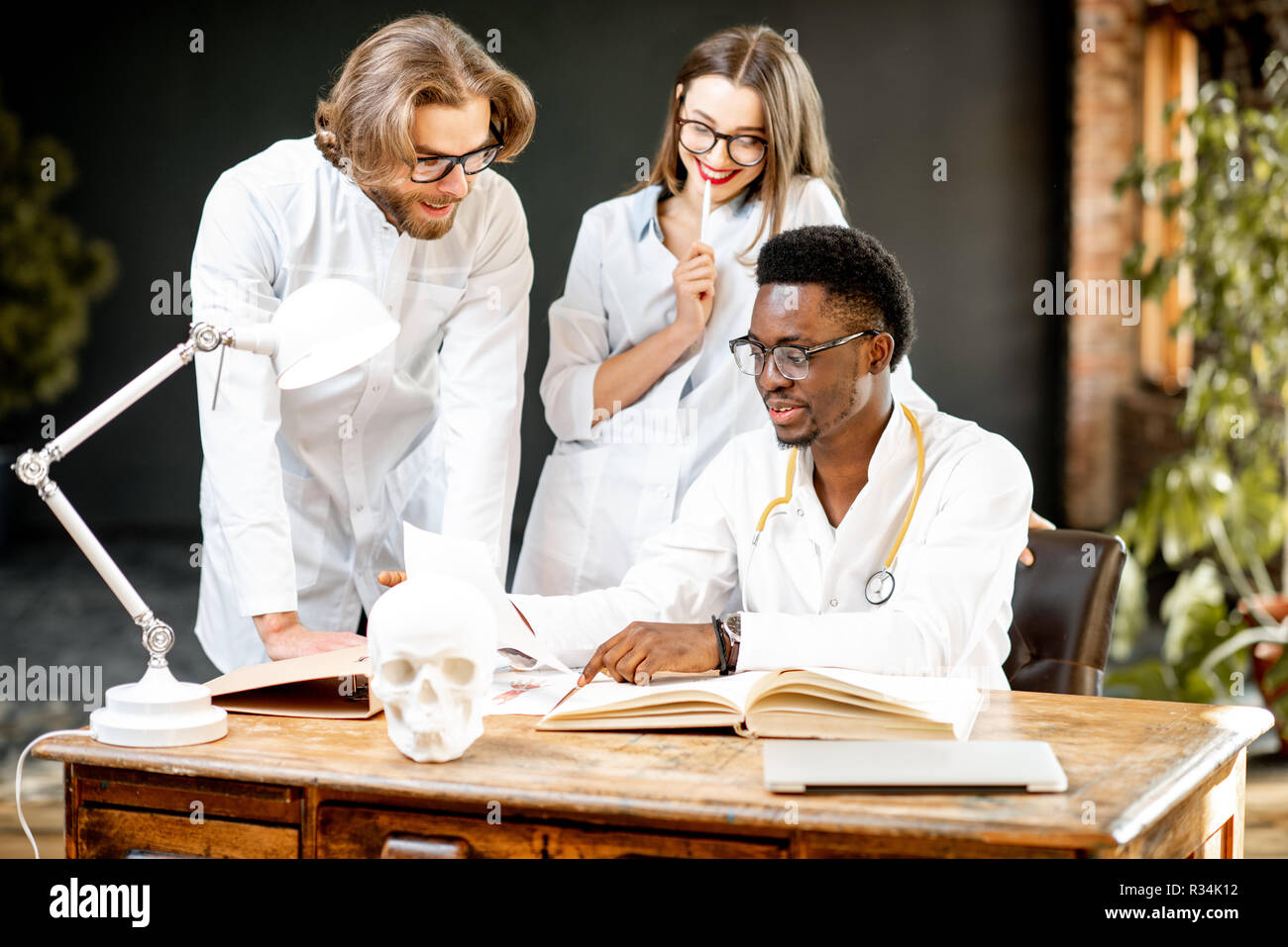 Gruppo di una giovane la multietnicità medici o di studenti di medicina in uniforme lavora con libro e disegni sul tavolo in ufficio o a scuola Foto Stock