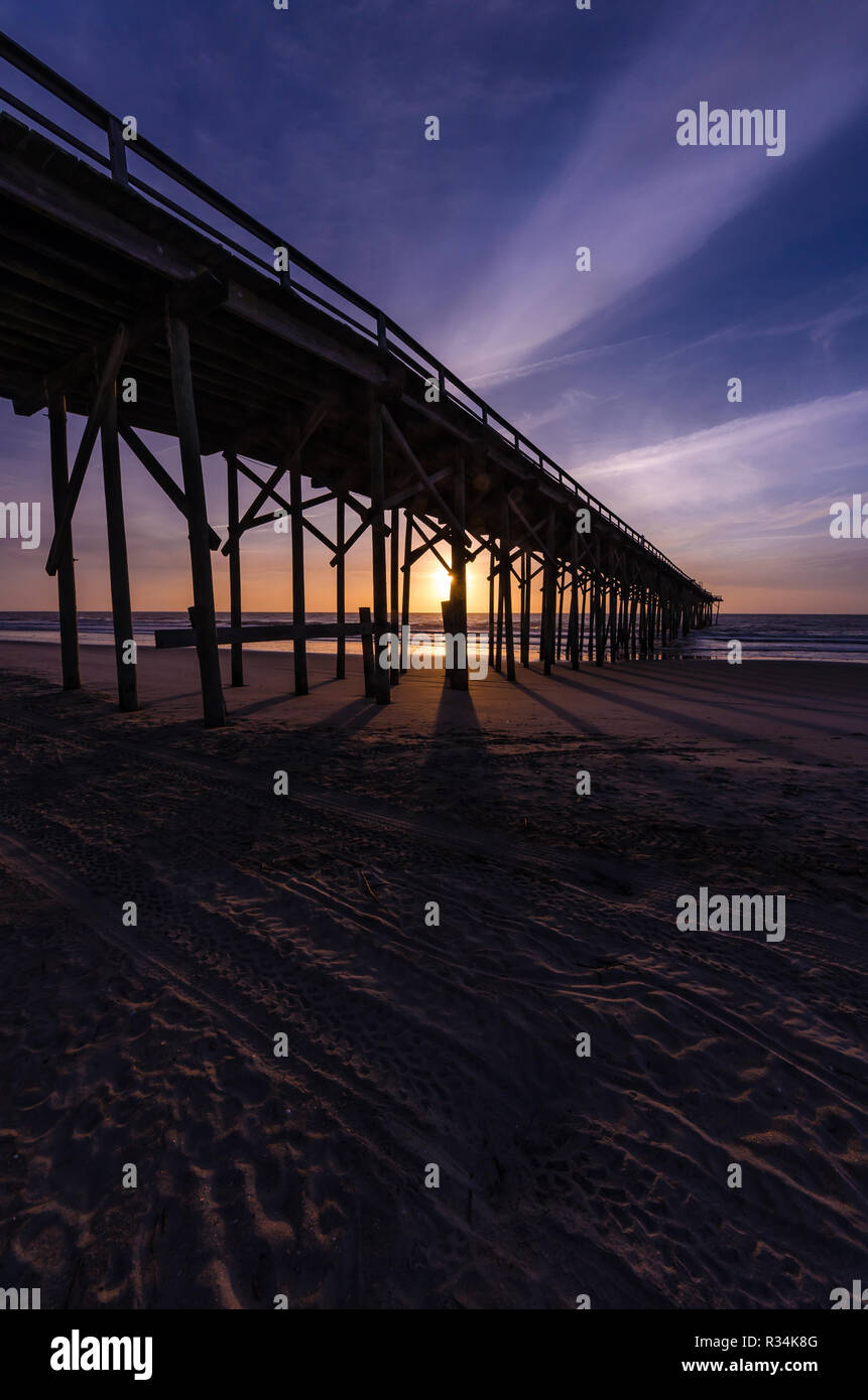 I raggi di luce durante il sunrise dietro un molo lungo la spiaggia Foto Stock