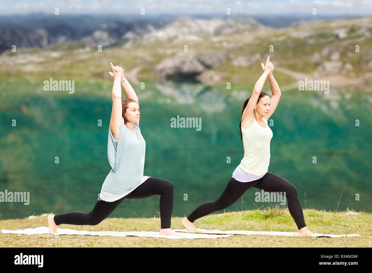 Due donne a fare yoga nella parte anteriore di un lago di montagna nelle Alpi Foto Stock