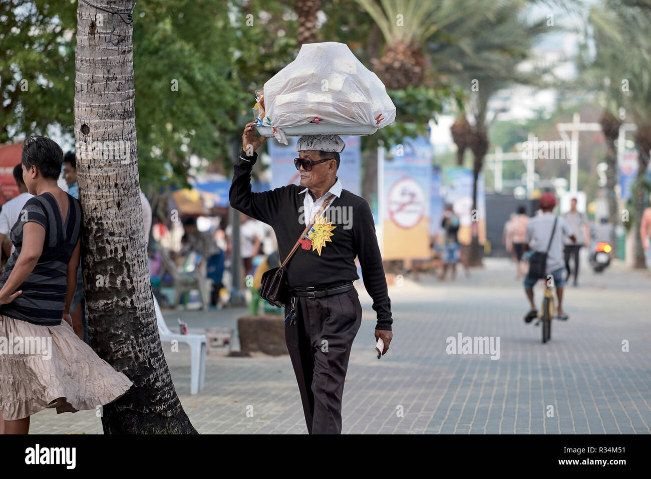 Thailandia street food vendor portando la sua mercanzia sulla sua testa e insolitamente ben vestita per questo lavoro. Foto Stock