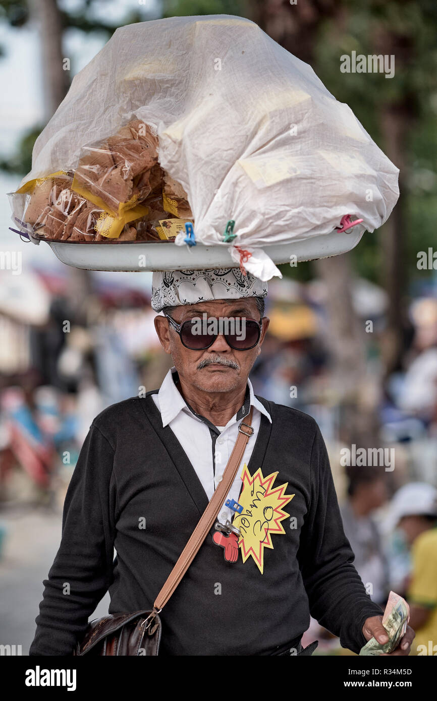 Thailandia street food vendor portando la sua mercanzia sulla sua testa e insolitamente ben vestita per questo lavoro. Foto Stock