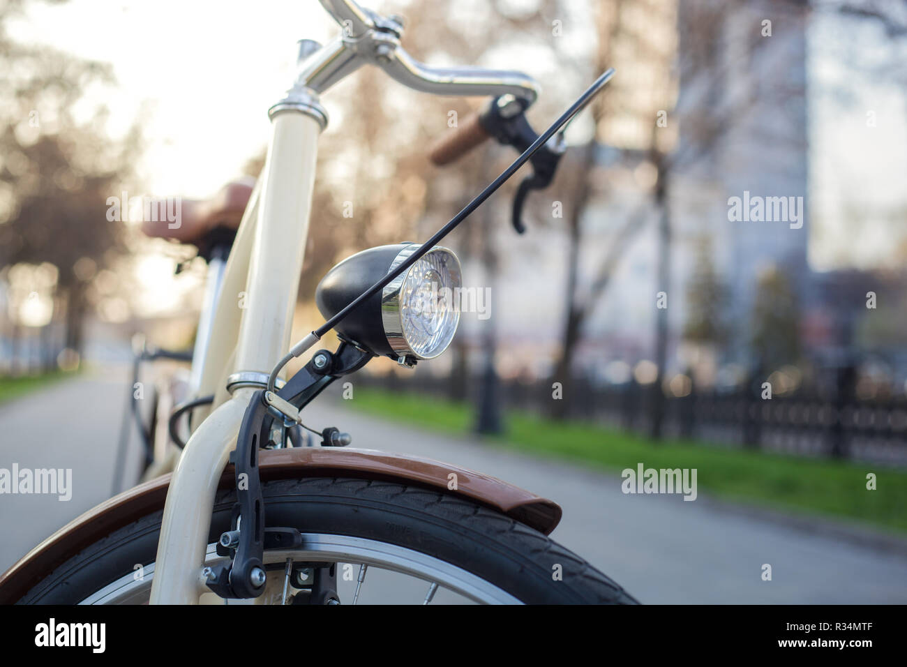 Bicicletta di colore beige con una lanterna su un viale con erba verde in primavera Foto Stock