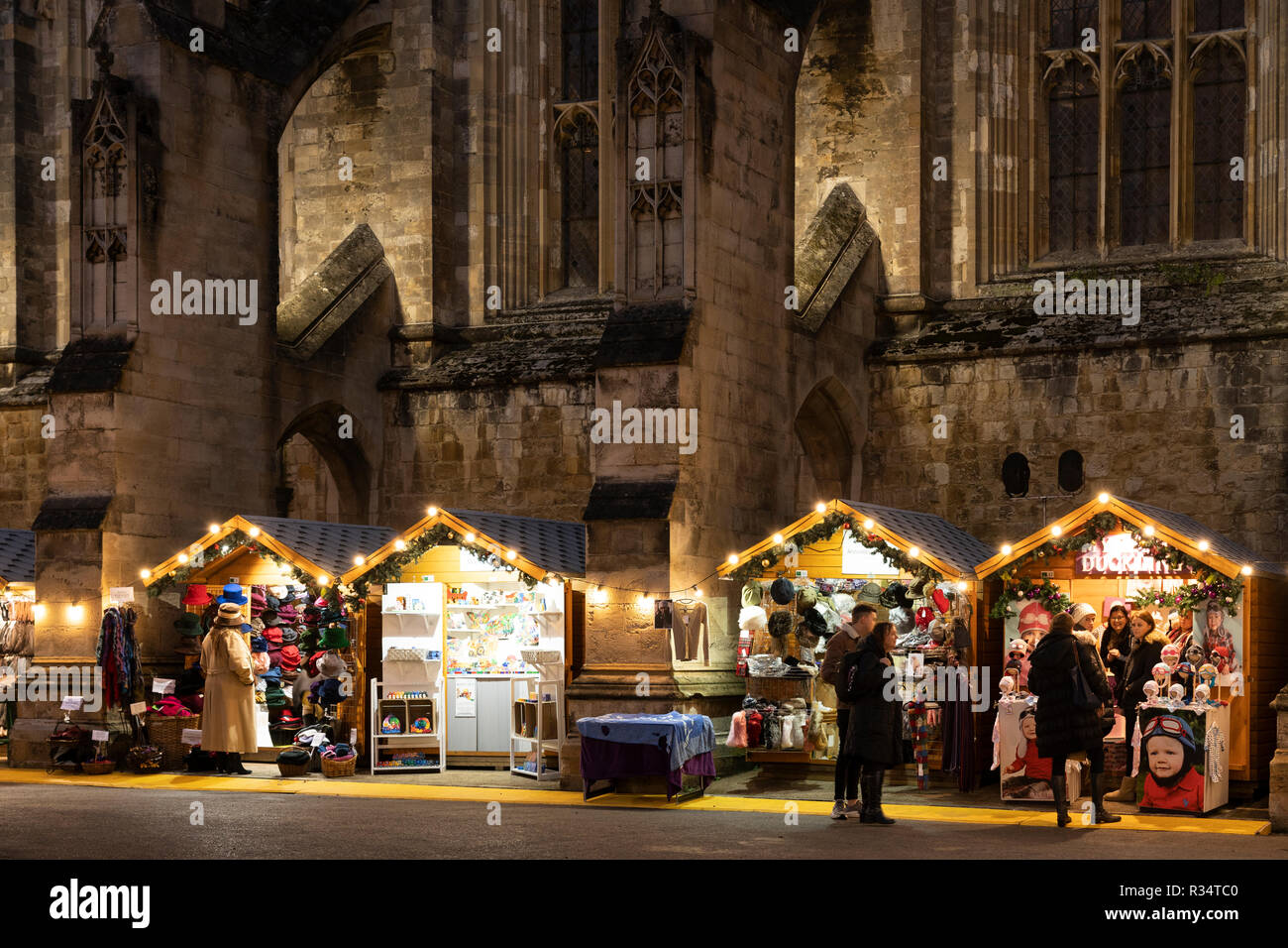 La cattedrale gotica di Winchester di notte e il mercatino di Natale nella città medievale di Winchester con gli acquirenti di Natale che navigano in chalet di legno. Inghilterra Foto Stock