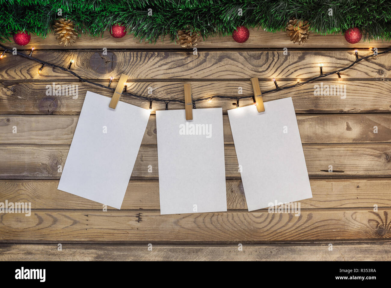 Auguri di Natale su un foglio bianco appeso su una ghirlanda con clothespins su uno sfondo di legno decorato con tinsel verde e rosso dei giocattoli Foto Stock