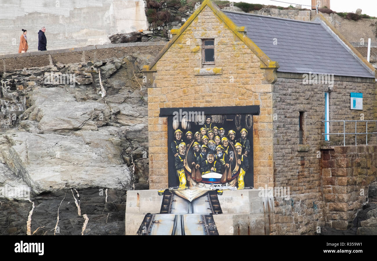 Dipinto a mano porta di molte facce della vecchia stazione di salvataggio, ora una galleria d'arte, a Porthleven con due persone passato a piedi sulla strada al di sopra. Foto Stock