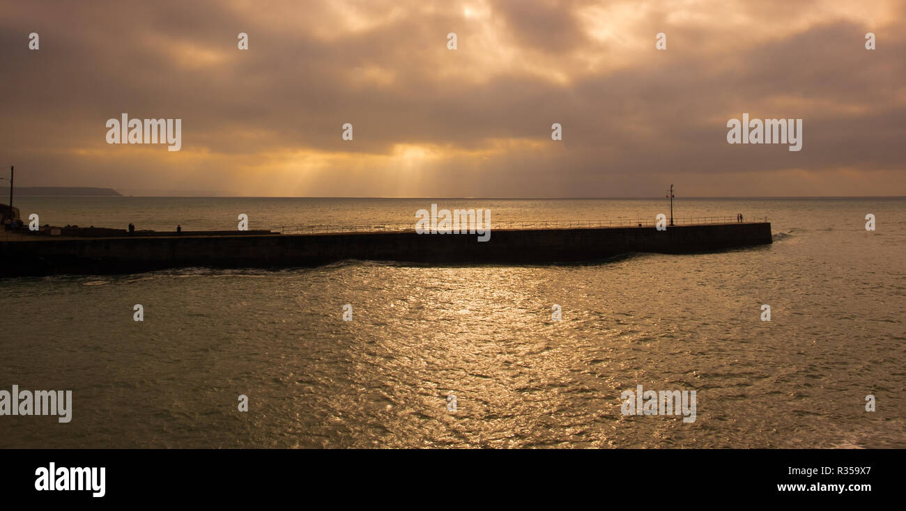 Digital golden enhanced nuvole sopra porto Porthleven parete con luce che colpisce attraverso e scintillanti sull'acqua. Foto Stock