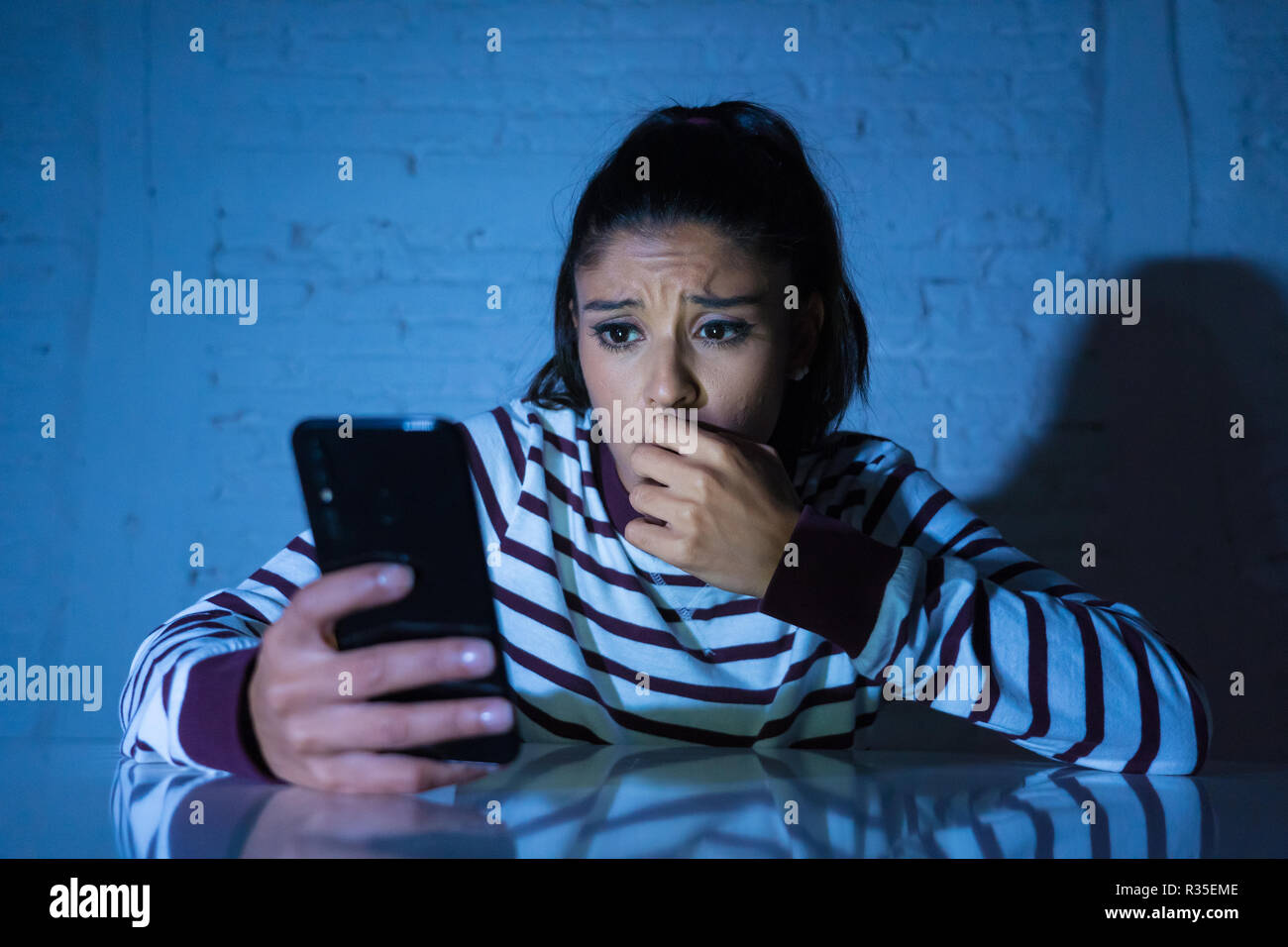 Frightened adolescente o giovane donna utilizzando smart telefono cellulare come internet cyberbullismo dal messaggio sgambate abusato della vittima. Foto Stock