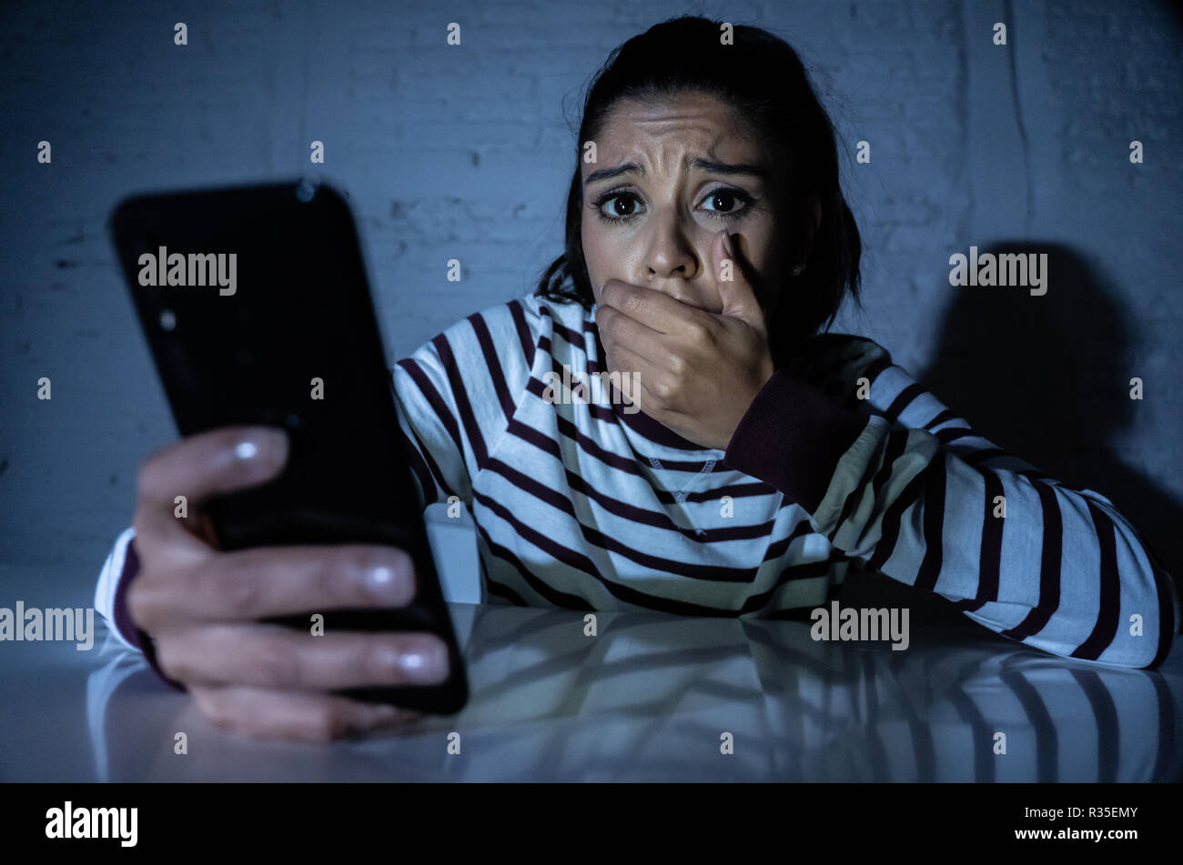 Frightened adolescente o giovane donna utilizzando smart telefono cellulare come internet cyberbullismo dal messaggio sgambate abusato della vittima. Foto Stock