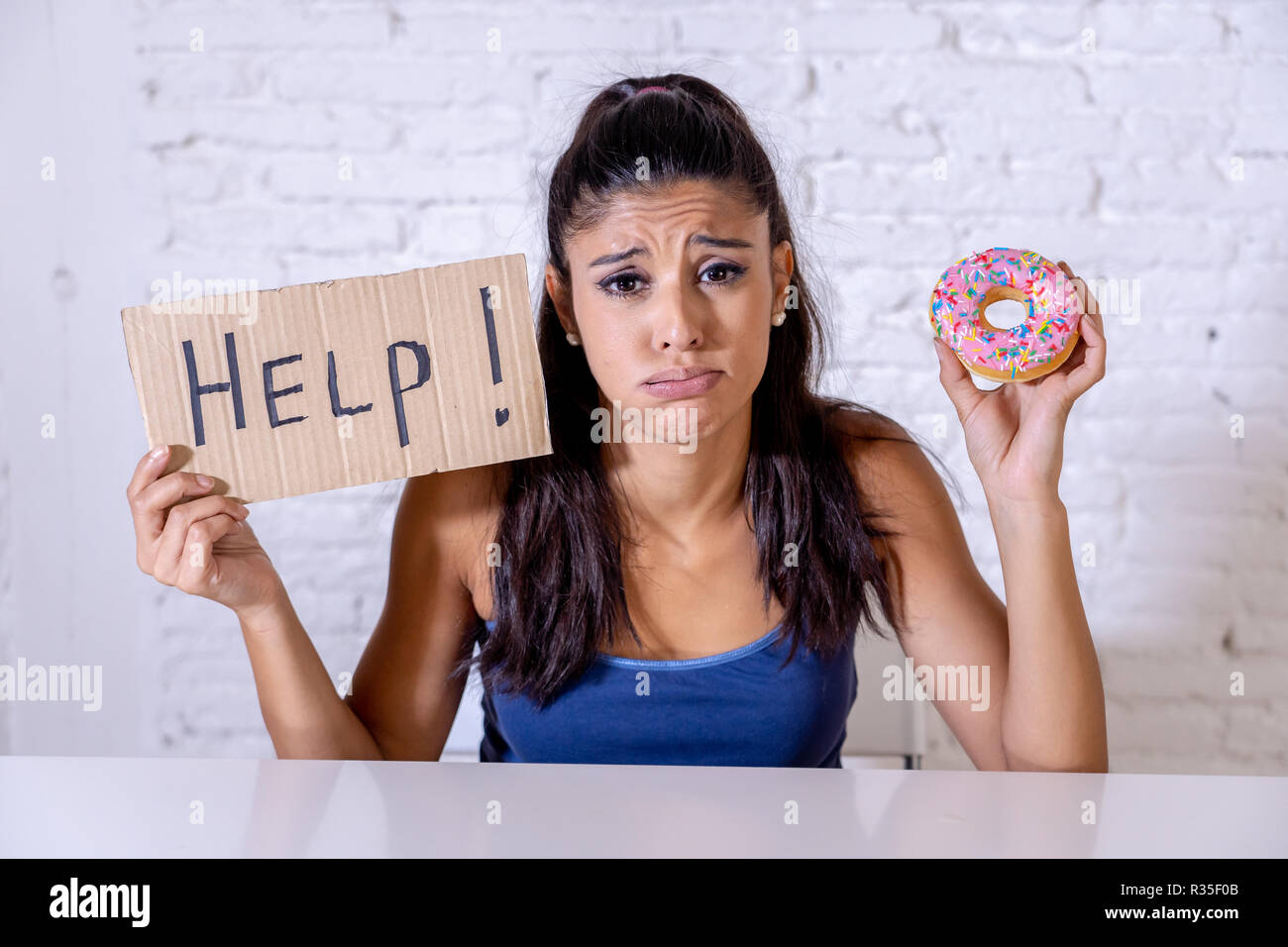 Giovani preoccupati latino sentimento donna tentati e colpevole che vogliono mangiare cioccolato e ciambelle per chiedere aiuto nella dieta calorie zucchero nutrizione della tossicodipendenza un Foto Stock