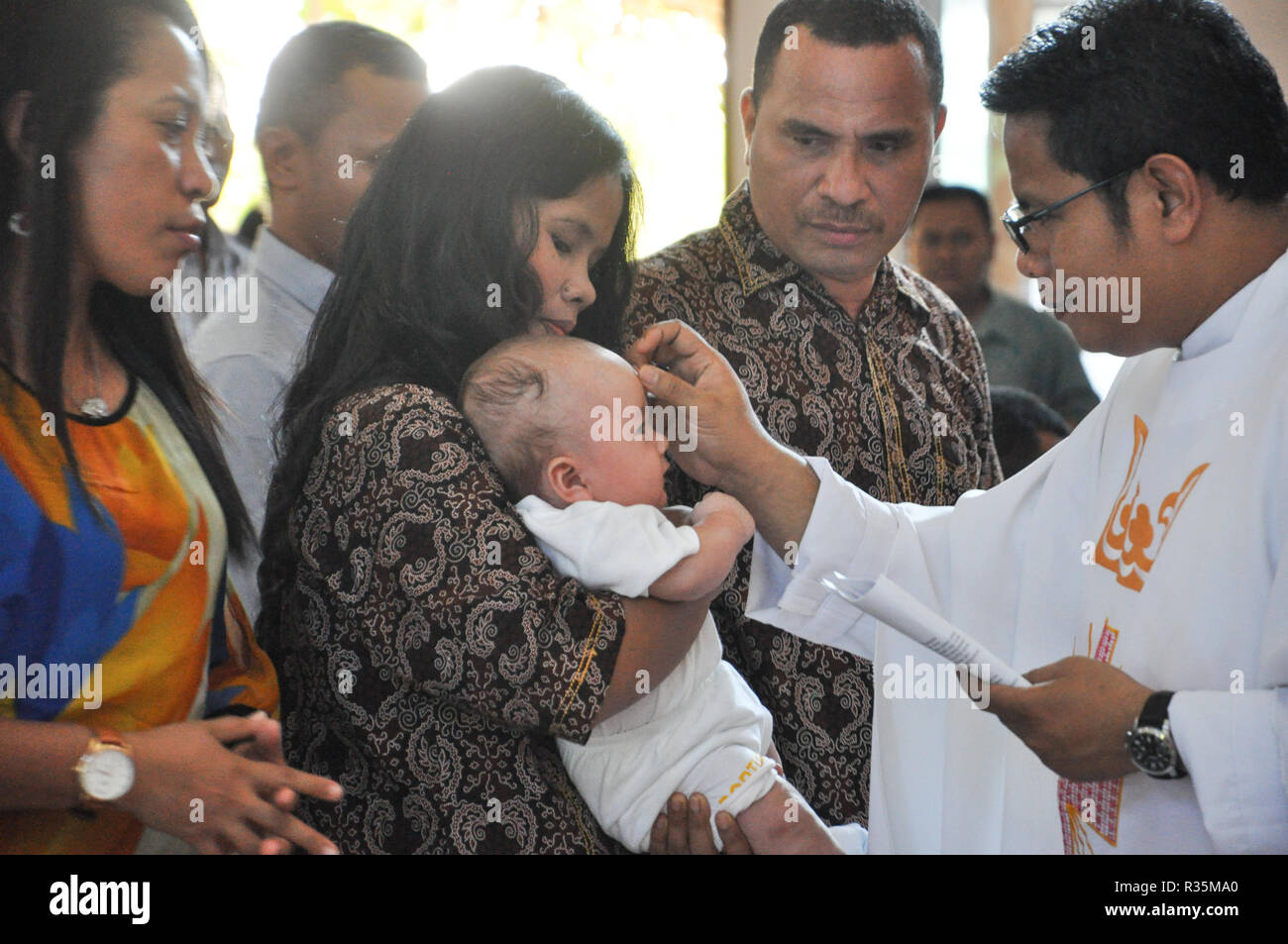 Batam, Indonesia. Un sacerdote rende un marchio di croce sulla fronte del bambino battezzato. Foto Stock