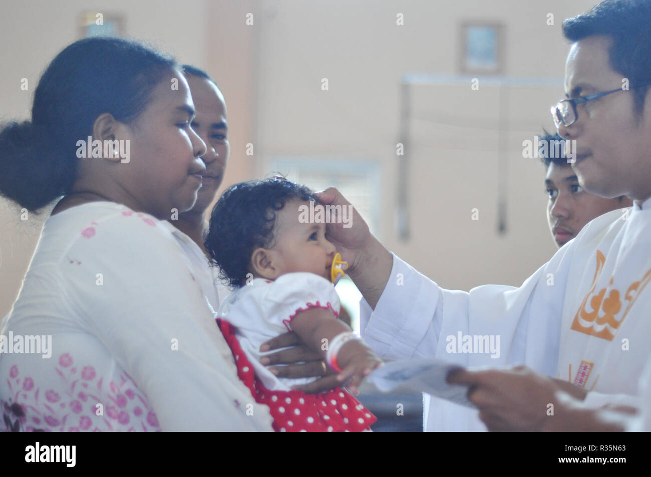 Batam, Indonesia. Un sacerdote rende un marchio di croce sulla fronte del bambino battezzato. Foto Stock