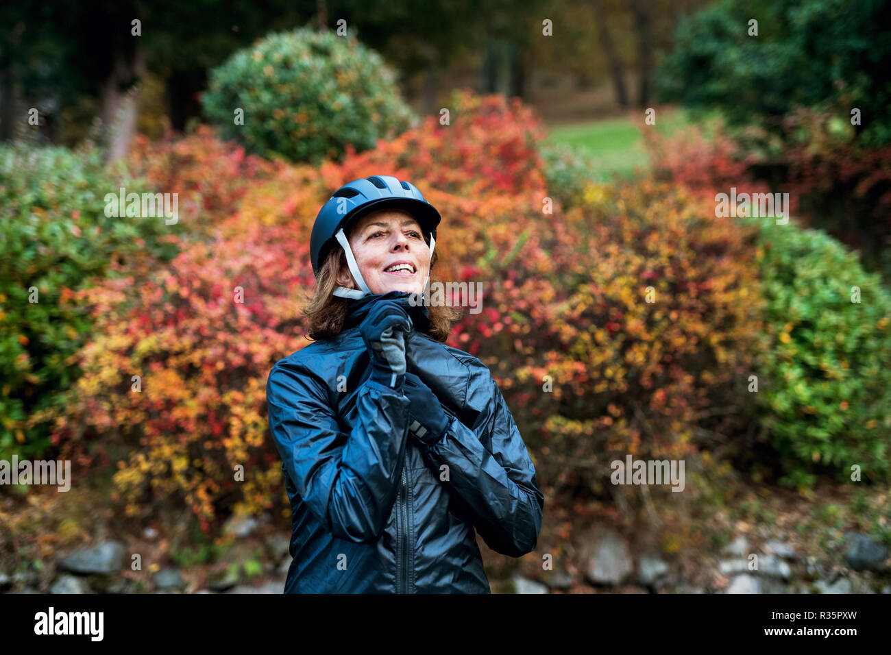 Active senior woman standing all'aperto su una strada in natura, mettendo sul casco per bicicletta. Foto Stock