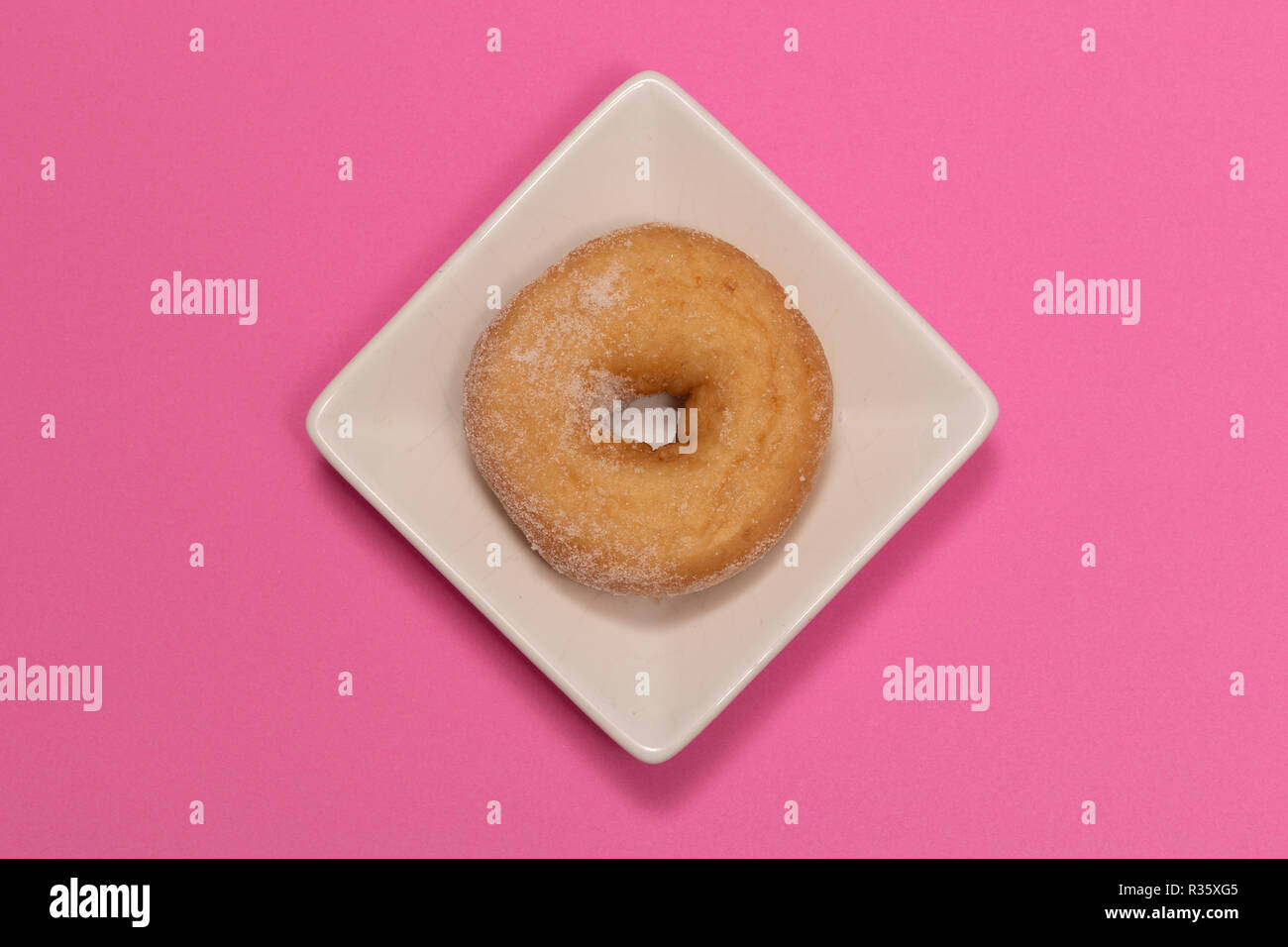 Zucchero ciambella rivestito su una piastra bianca con sfondo rosa Foto Stock