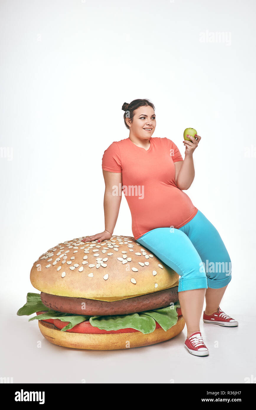 Bruna, divertente, paffuto donna siede su un enorme panino Foto Stock
