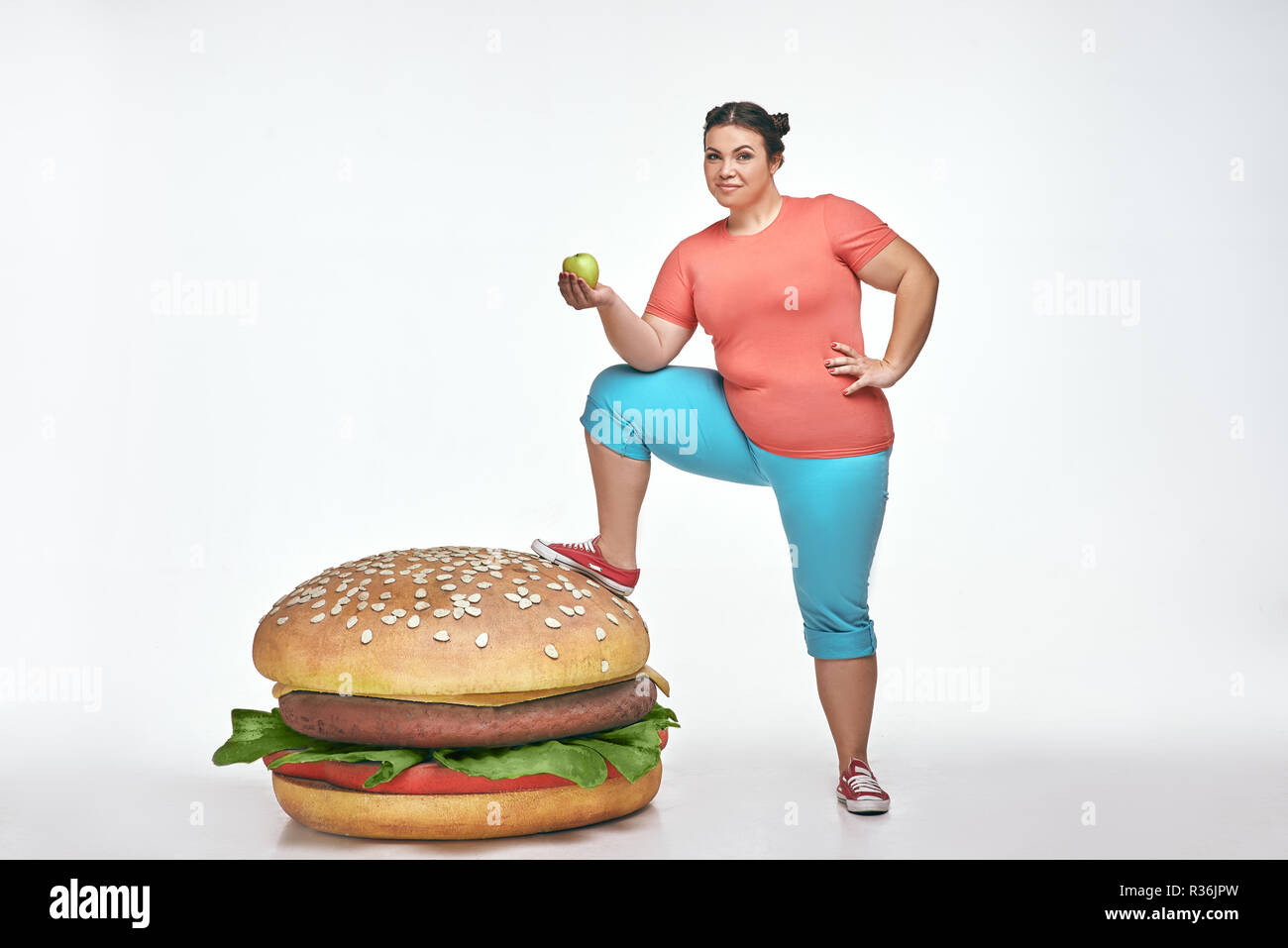 Bruna, divertente, paffuto donna mettere la sua gamba a un enorme panino Foto Stock